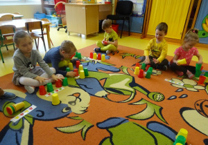 Dzieci układają kubeczki według wzoru na kartce.